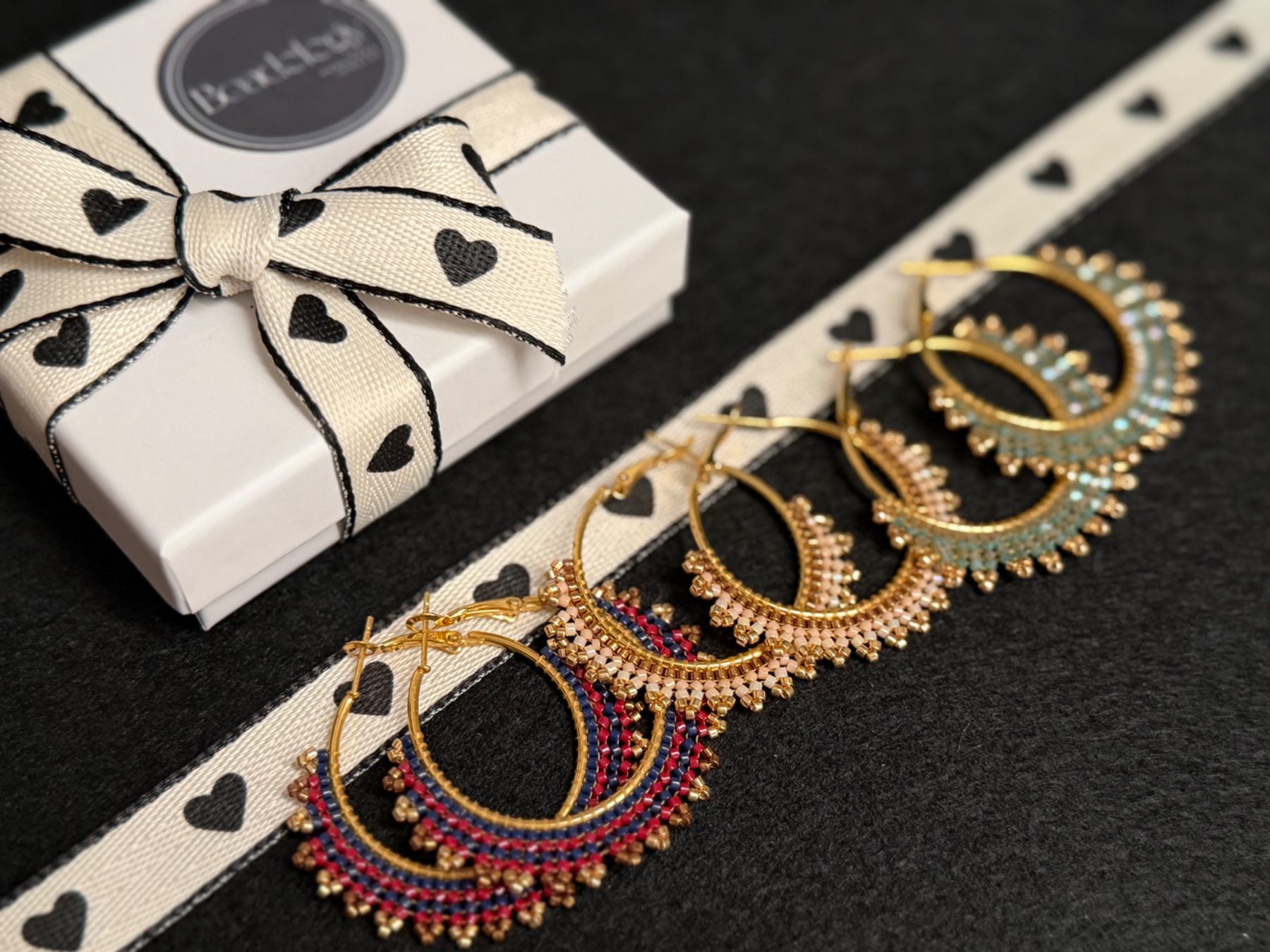 Three pairs of beaded gold hoop earrings next to a Beadology gift box
